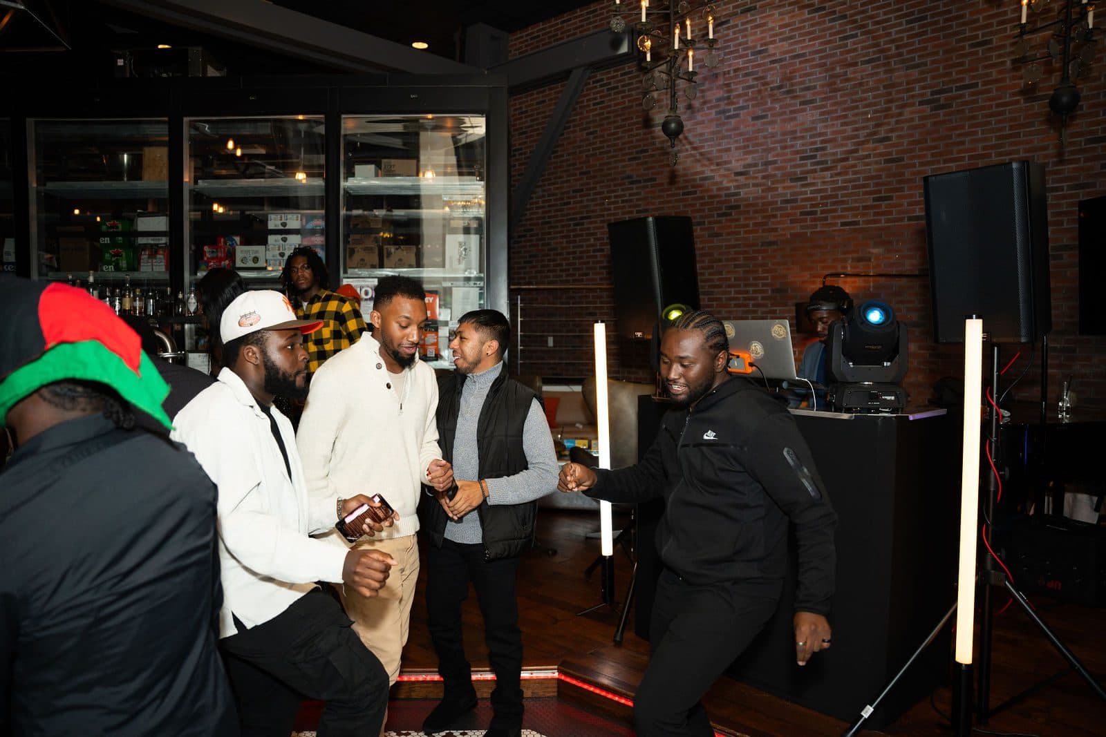 Guests dancing in front of a DJ booth with speakers and light bars in a brick-walled bar