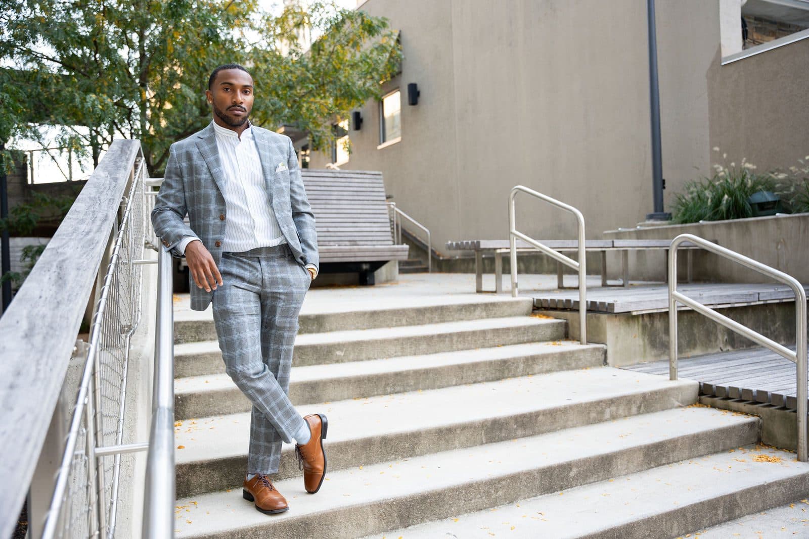 Portrait in a gray plaid suit leaning on a railing at the top of outdoor stairs