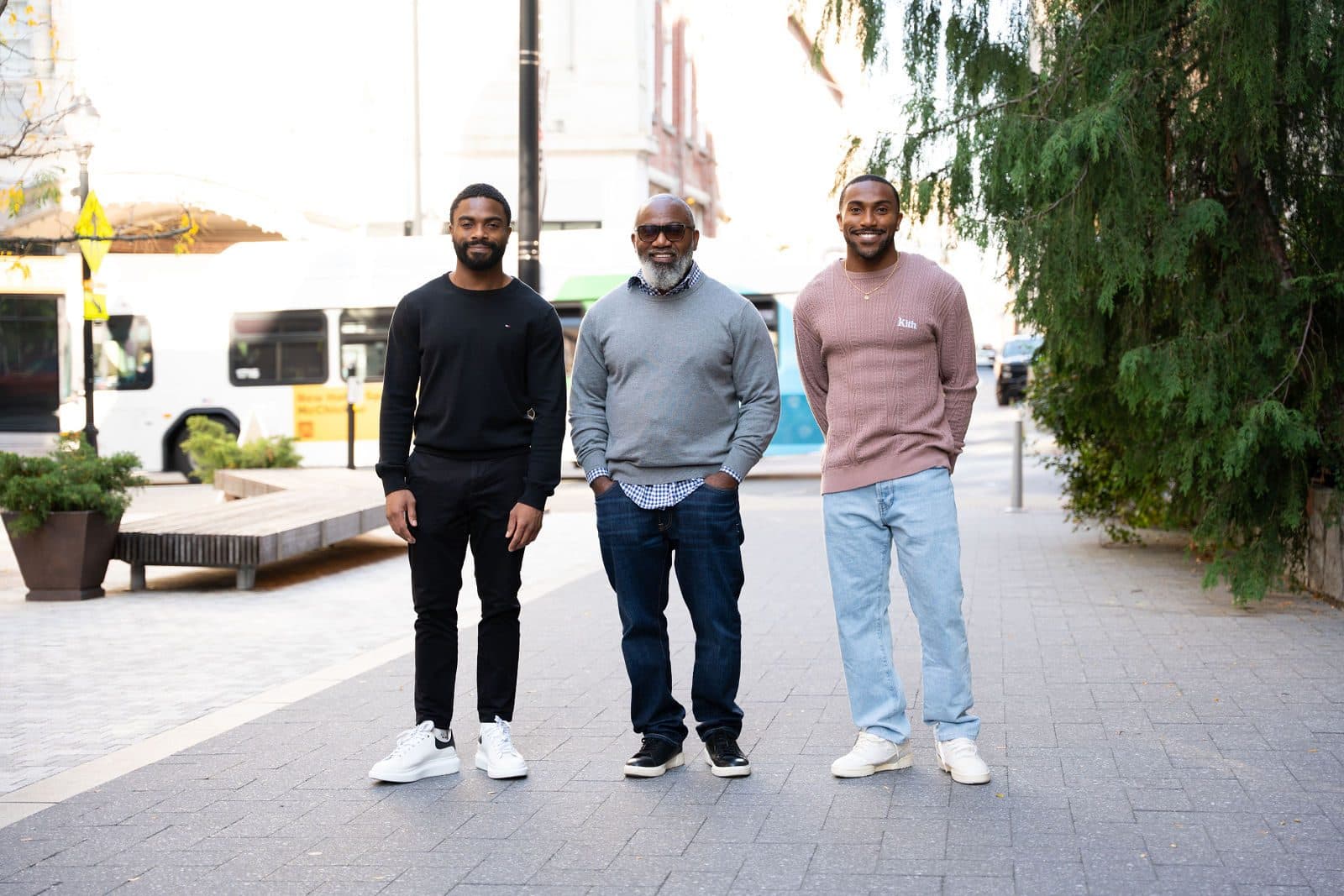 Three men in casual sweaters and jeans standing together on a city pedestrian street
