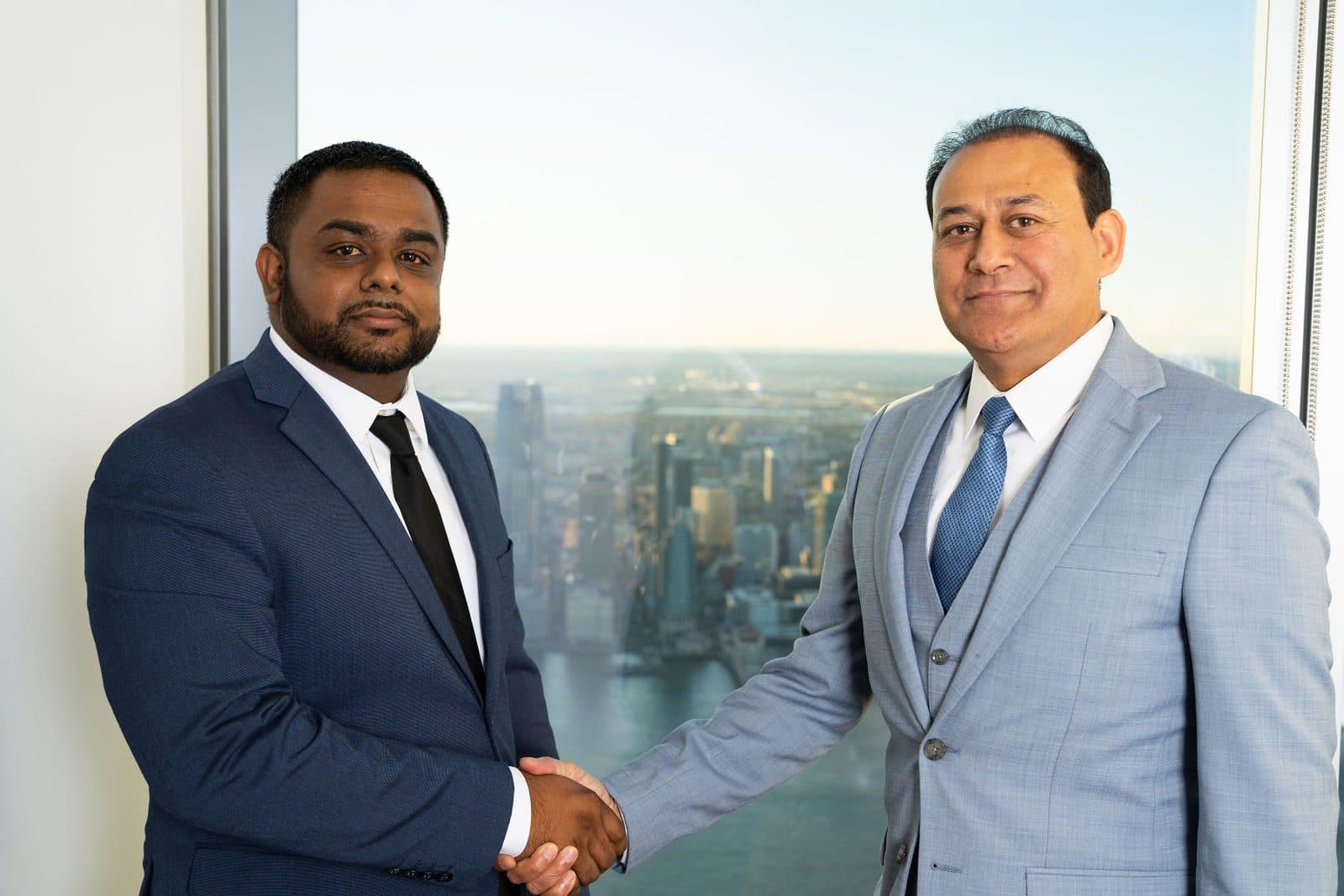 Two executives shaking hands in front of a window overlooking the city