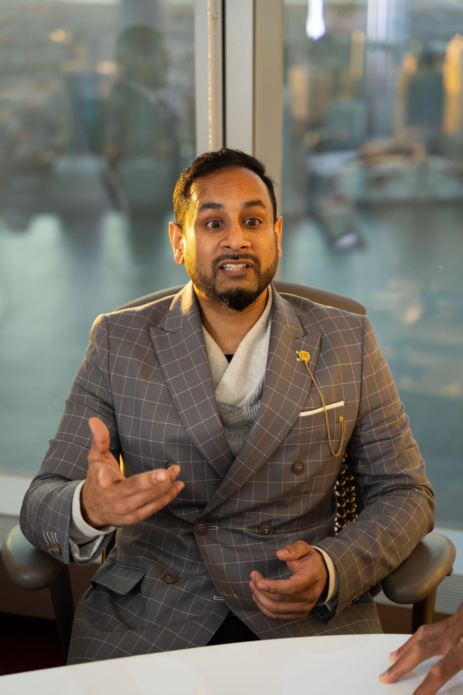 Executive in a gray plaid suit speaking during a meeting by a window