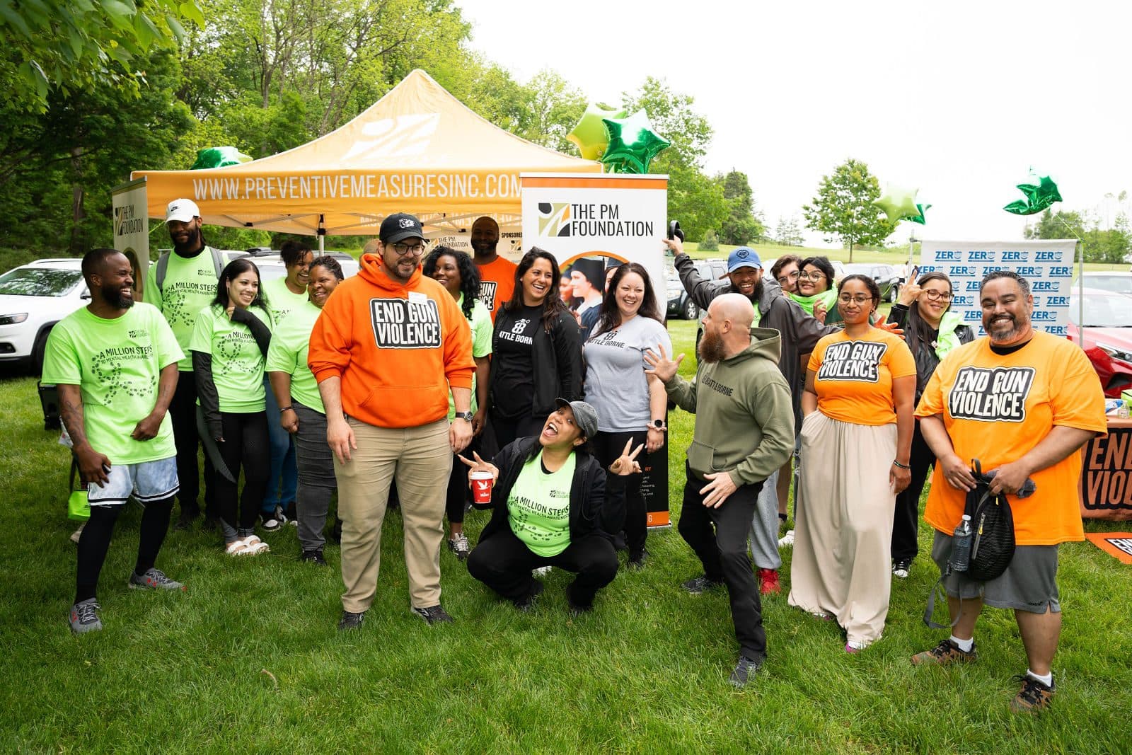Group in green and orange event T-shirts gathered on the grass in front of a canopy tent and foundation banners