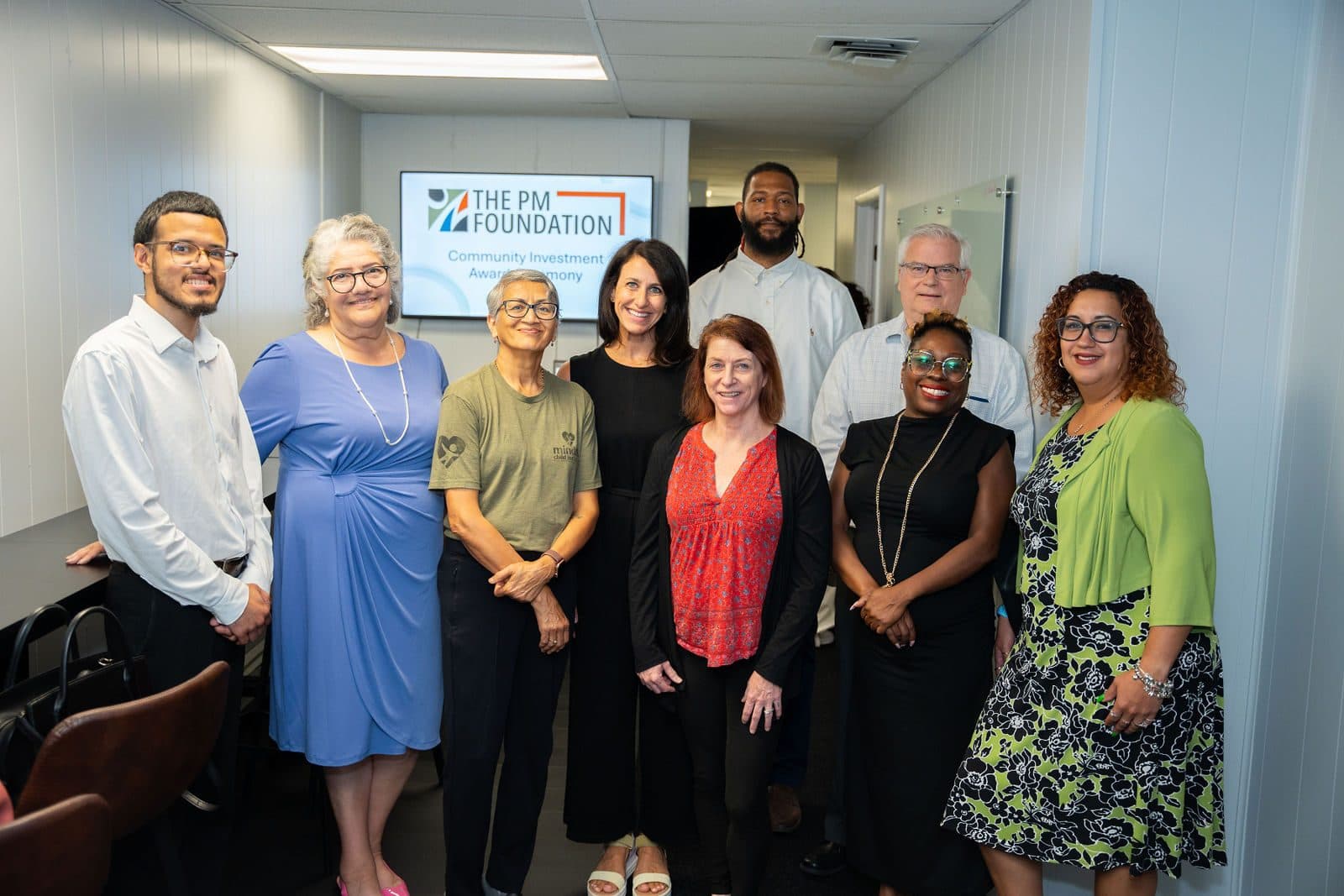 Group posing in an office hallway in front of a screen showing The PM Foundation logo