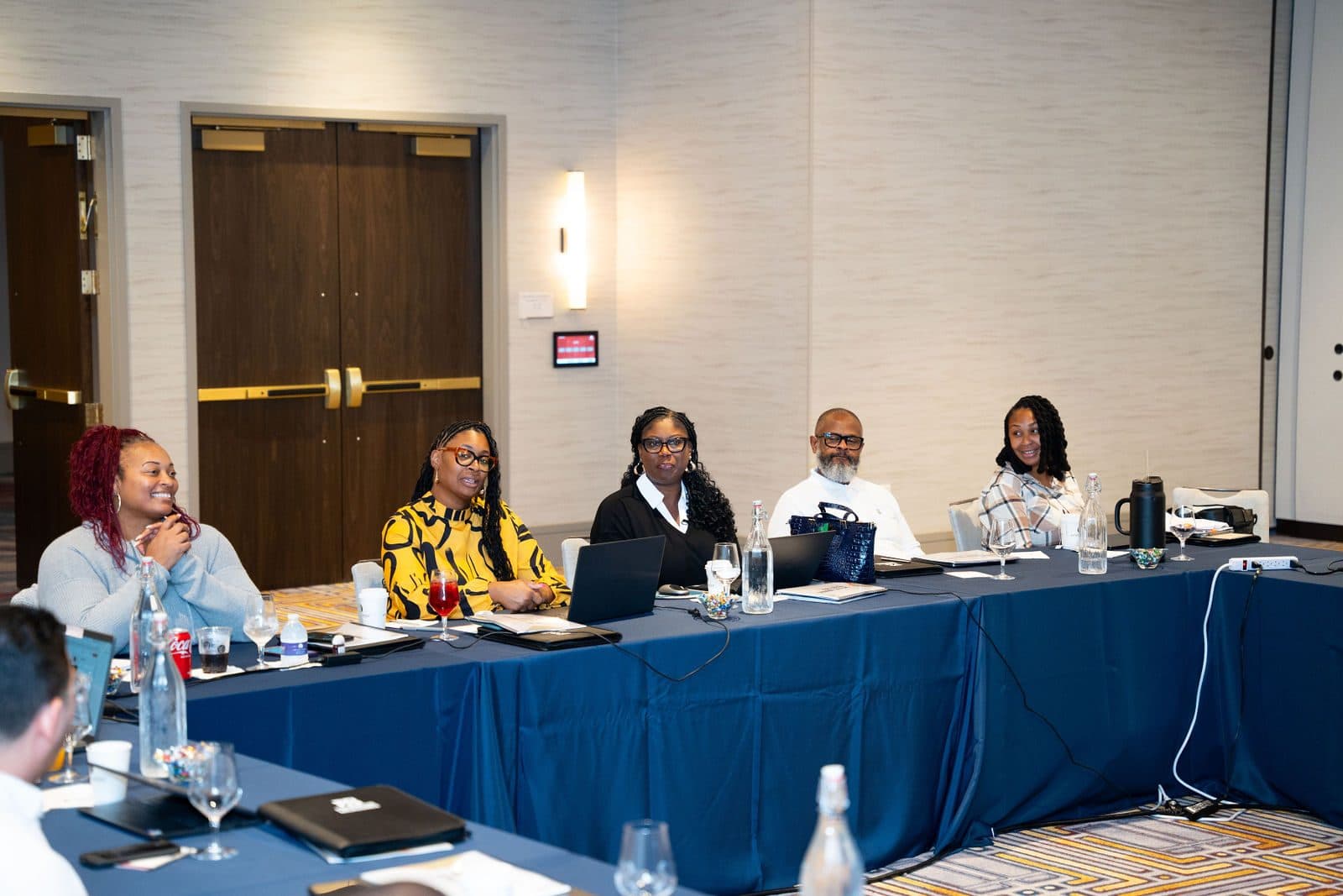 Attendees smiling at a blue-draped conference table with laptops and water glasses during a management retreat