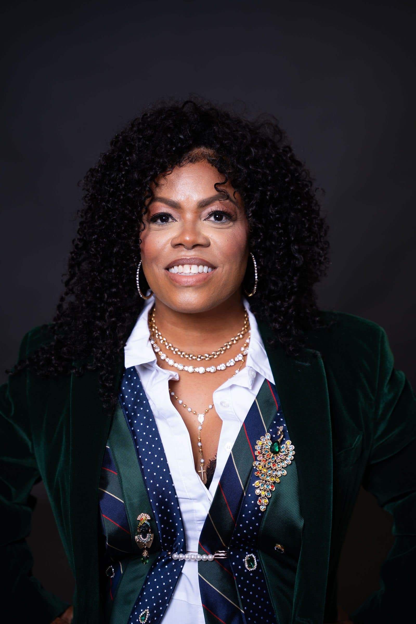 Portrait in a green velvet blazer and pearl necklace against a dark backdrop