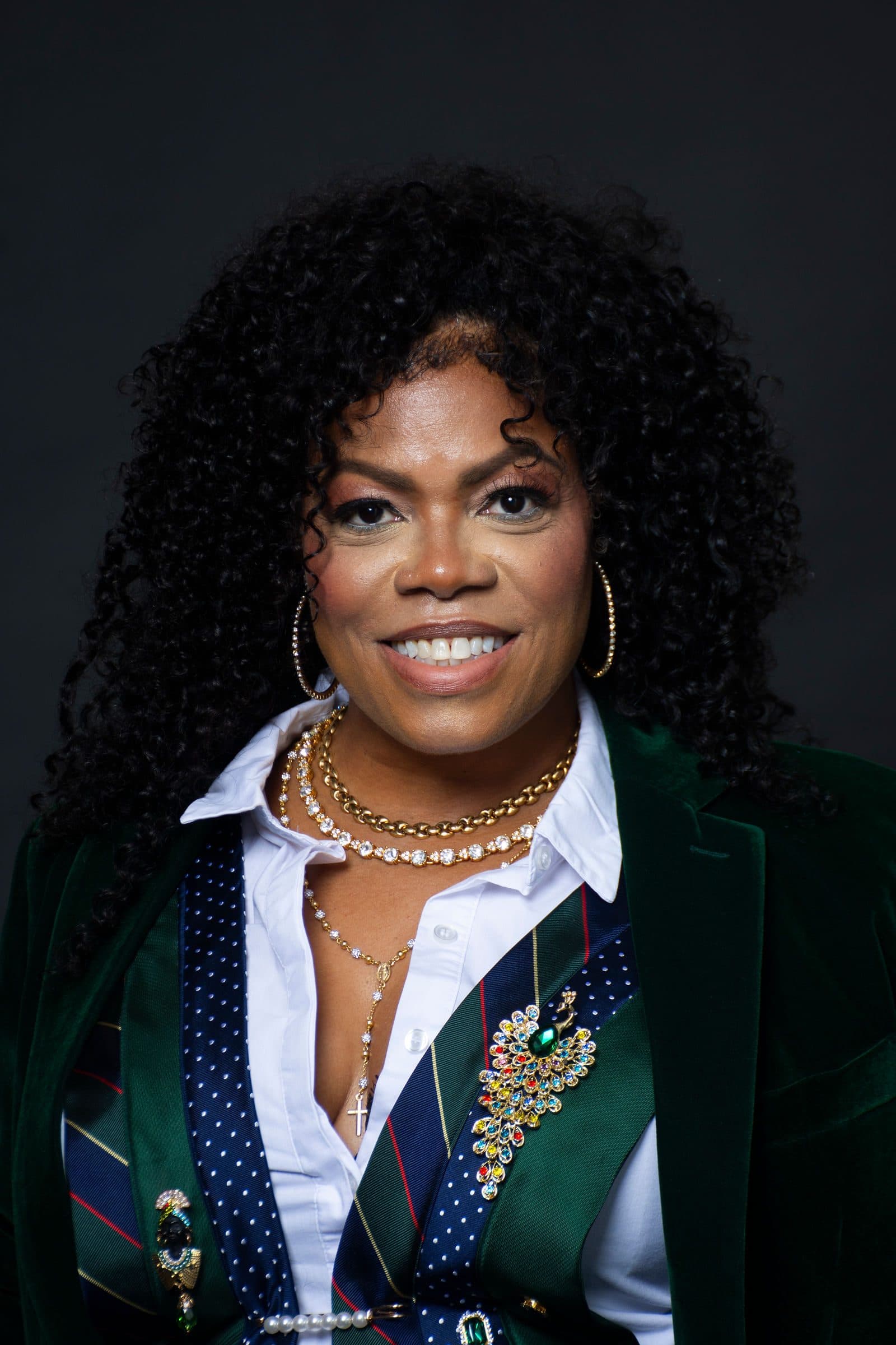 Close portrait in a white shirt and green patterned vest against a dark backdrop
