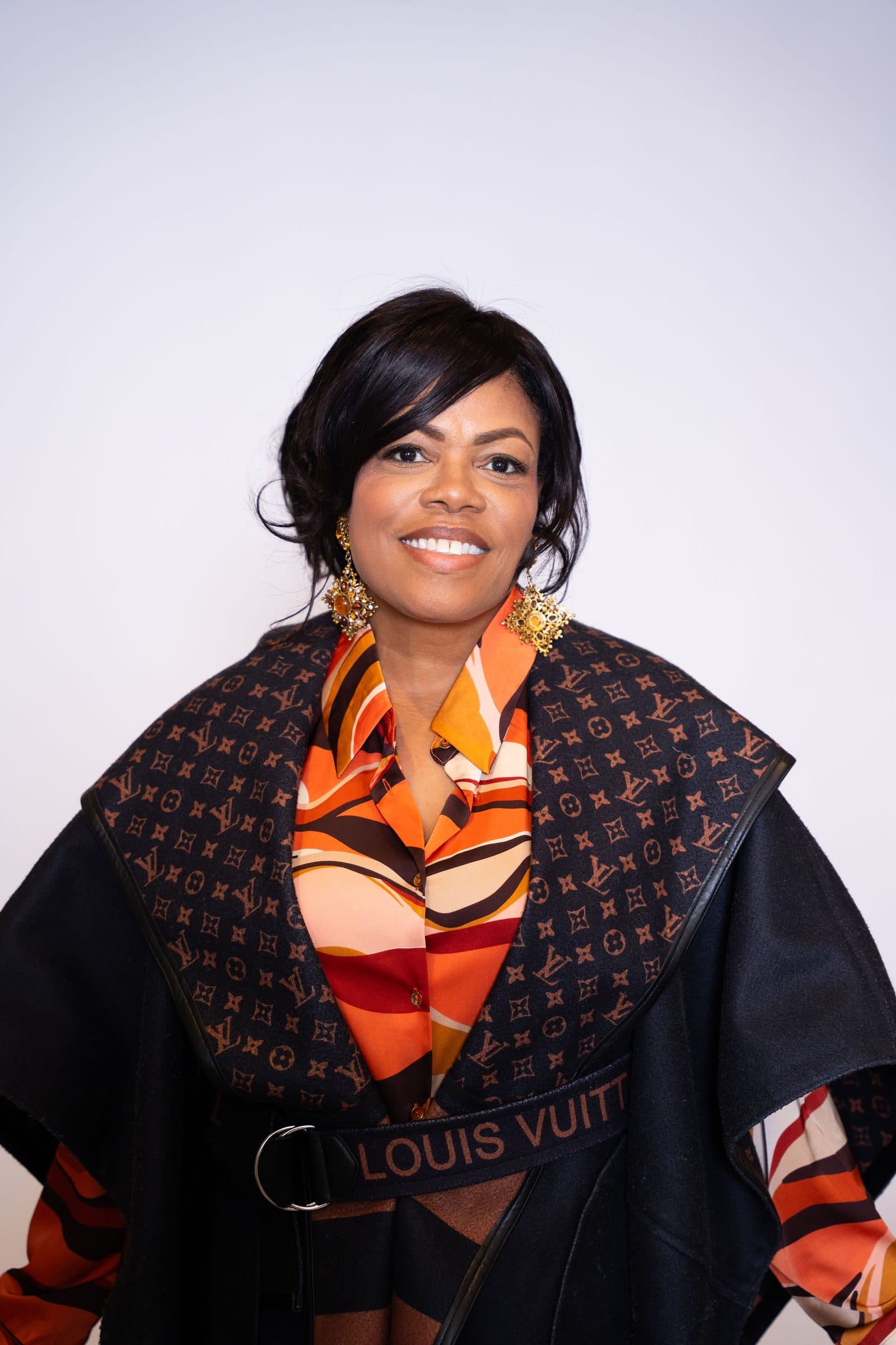 Studio portrait in a patterned cape and orange scarf on a white backdrop